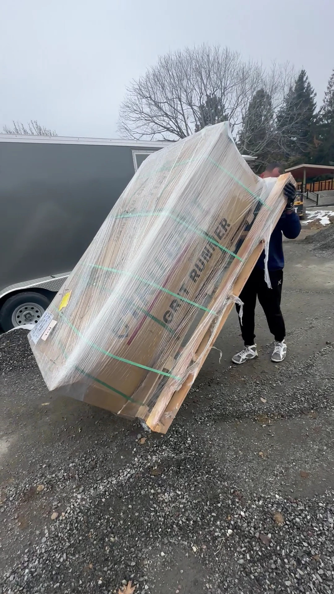 A shrink-wrapped pallet of boxed goods tipped up on its edge and walked across the gravel.