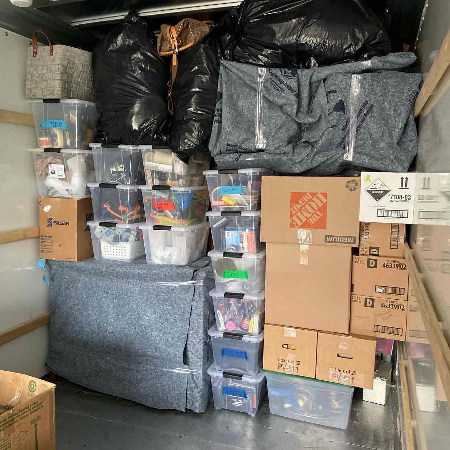A truck body packed wall to wall — labelled totes stacked square, bags and cartons fitted in around blanket-wrapped furniture.
